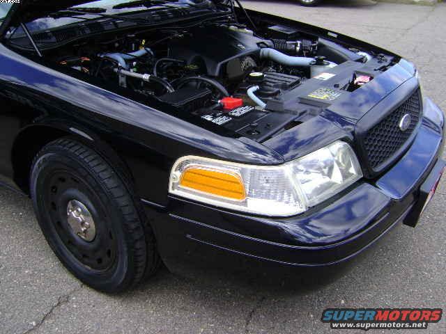 Front corner of a black 2003 Ford Crown Victoria with the hood open, showing the engine bay. The grille and headlight are visible
