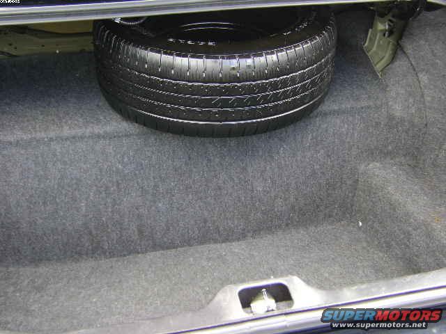 Spare tire in trunk of a car, carpeted interior, metal latch visible