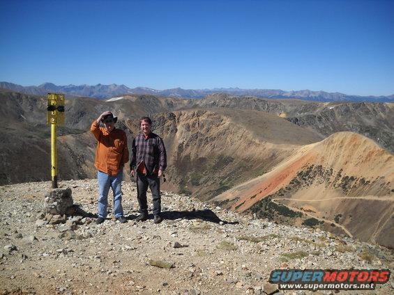 Two men stand on a rocky mountain peak under a clear blue sky