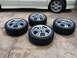 2003 Acura TL - Four aftermarket wheels and tires are displayed on a concrete surface, with the lower portion of a white vehicle visible behind them.