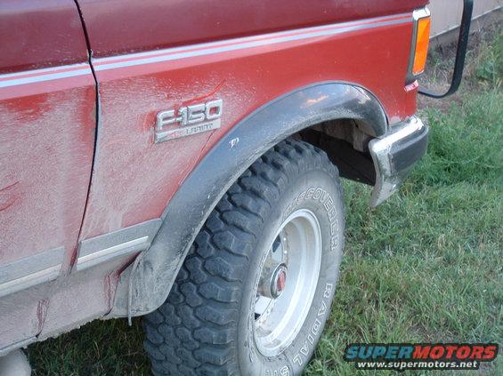 Red Ford F-150 side view, showing fender badge and tire. The truck is dusty