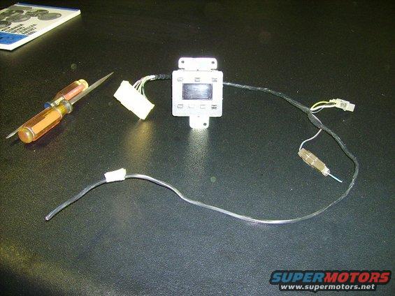 Car dashboard control module with wires and a screwdriver on a black surface