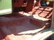 1964 Ford Fairlane - Interior floor pan of a car, primed red, with visible seat mounting points and transmission tunnel.
