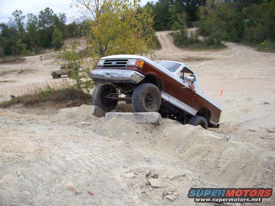 Ford F-Series truck climbing over rocks on a dirt trail. Another truck is visible in the background