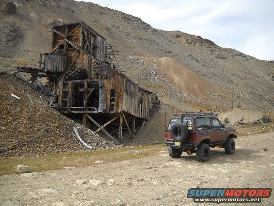 Brown Ford Bronco II with spare tire on rear, parked on dirt road near abandoned mine