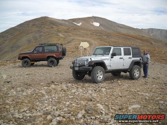 Brown SUV with roof rack and spare tire on back, parked on rocky terrain