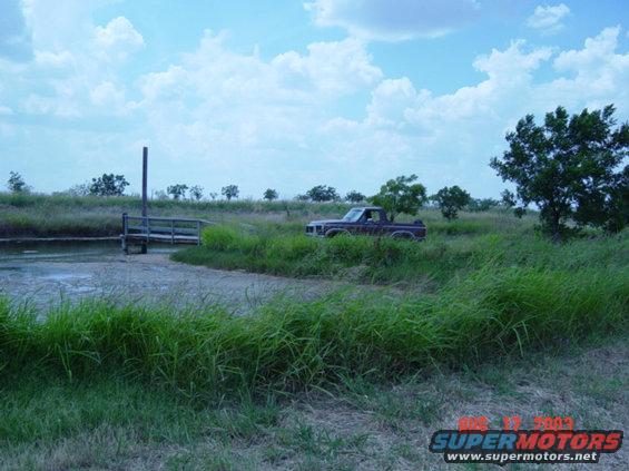 Dark red pickup truck in tall grass, 3q-front view. Appears to be from the early 1980s