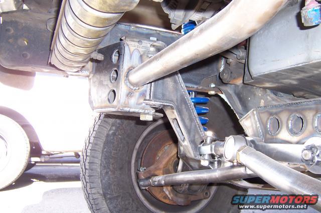Close-up of custom suspension components, including blue coil springs and fabricated metal brackets, attached to a vehicle's frame