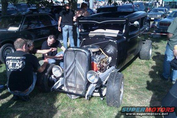 Black hot rod with exposed engine and chrome grille, viewed from the front