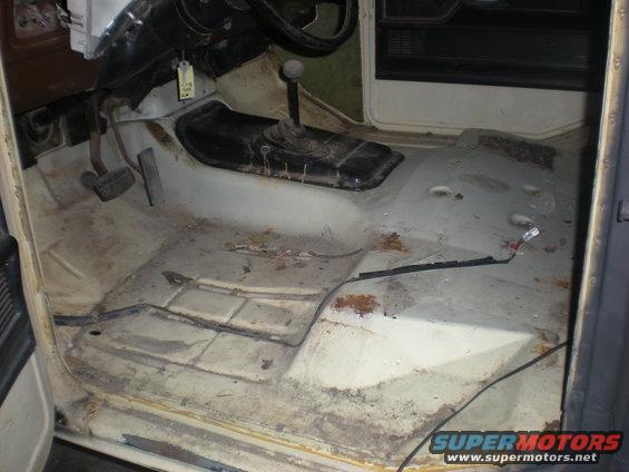 Interior floor of a vehicle, showing pedals, transmission tunnel, and bare metal with some rust