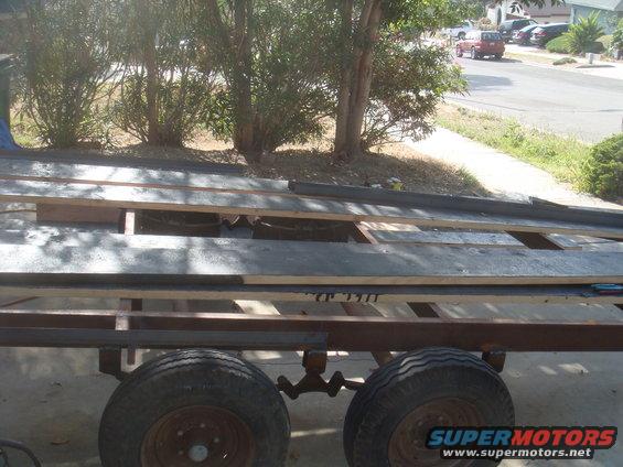 Trailer frame with wooden planks loaded on top. Two wheels visible