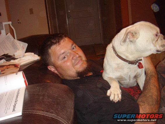 Man with beard holding a white dog on a brown leather couch