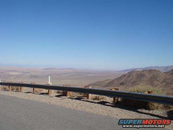 View of a wide desert valley from a roadside overlook with a guardrail in the foreground
