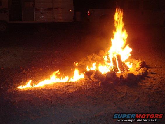 Campfire burning at night with a trailer and truck in the background