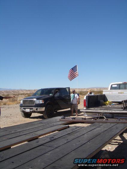 Black Ford F-150 pickup truck parked next to a trailer, with an American flag flying