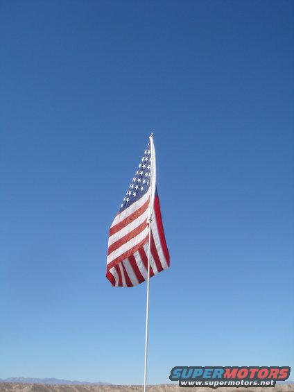 American flag waving against a clear blue sky, with a distant desert landscape below