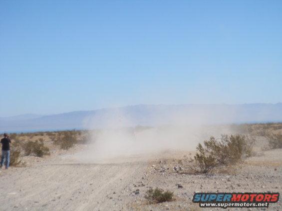 Off-road vehicle kicking up dust on a dirt road in the desert