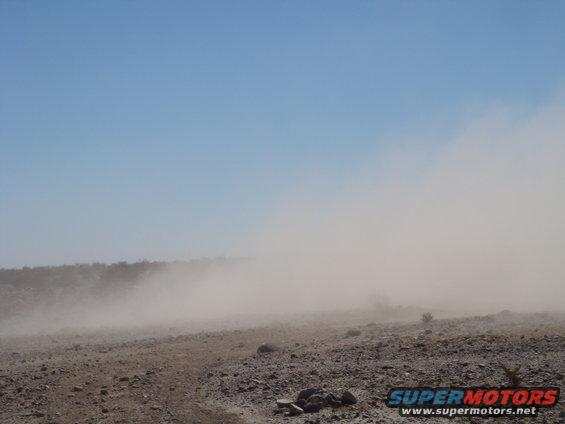 Dust cloud obscuring desert terrain under a clear blue sky