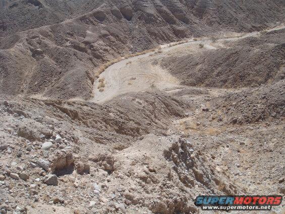 Desert canyon with a winding dirt road. A small vehicle is visible in the distance
