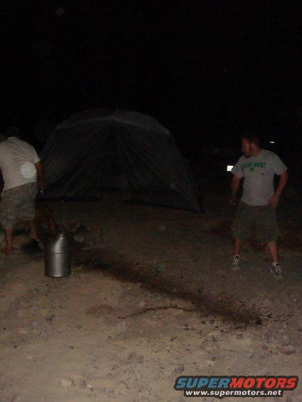Two guys and a tent at night, with a metal container on the ground