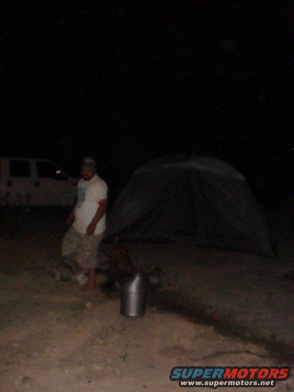 White van parked on dirt ground at night, with a person standing near a tent