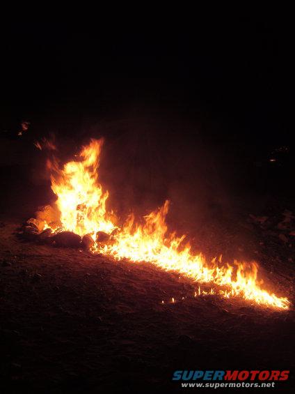 Fire burning on a dark, barren landscape with a Supermotors logo in the corner
