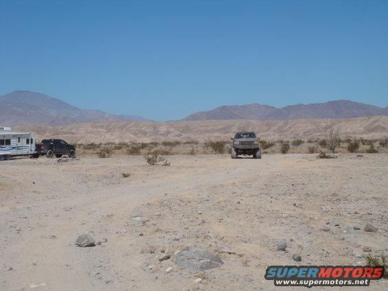 Desert scene with a lifted truck in the foreground and a trailer with a black SUV in the background
