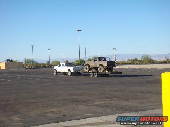 1987 Ford Bronco on trailer, towed by Ford F-150 pickup. Both vehicles are in a parking lot