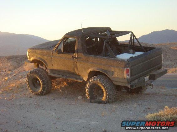 Brown 1992 Ford Bronco with off-road modifications, including a roll cage and large tires, parked on a dirt road