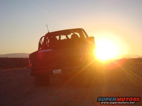 Dark SUV with soft top removed, rear view, California license plate 3SF319, parked in desert at sunset