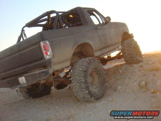 Modified 1992 Ford Bronco with roll cage and large tires climbing a dirt hill