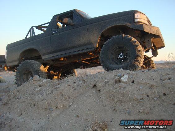 1992 Ford Bronco with large tires and roll cage climbing a dirt mound
