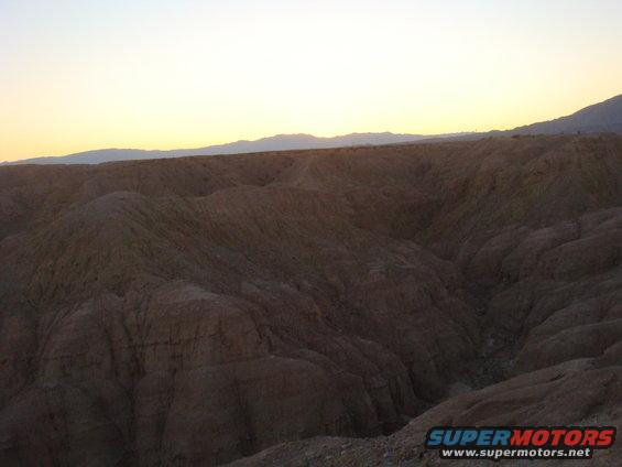 Desert landscape with eroded hills and mountains at sunset
