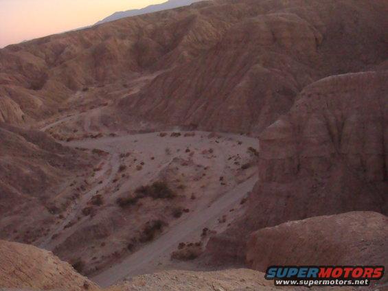 Desert landscape with a dirt road winding through hills. Supermotors.net logo visible