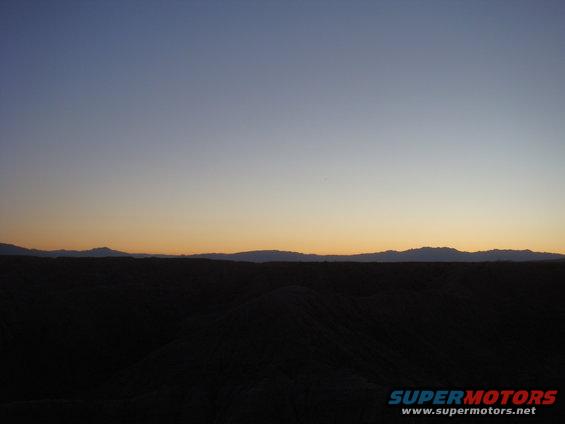 Desert hills and mountains under a gradient sky at dusk. Supermotors.net logo in lower right
