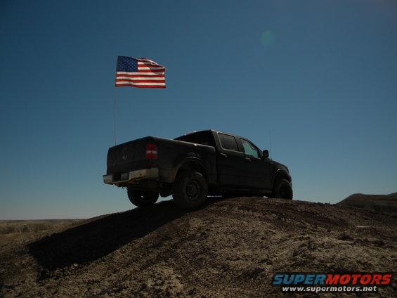 Dark pickup truck on a dirt hill with an American flag flying