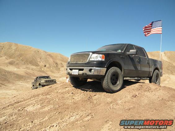Black pickup truck with an American flag on a pole, parked on a dirt hill