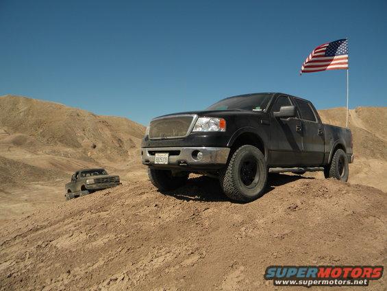 Black pickup truck with American flag flying in desert landscape