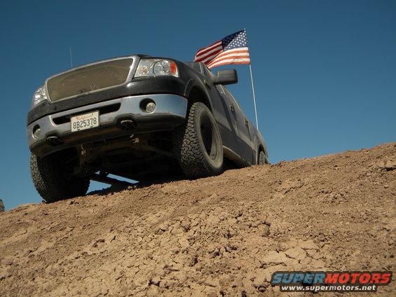 Black Ford F-150 pickup truck with American flag on a dirt hill