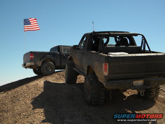 Black Bronco and pickup truck on a dirt hill with American flag flying
