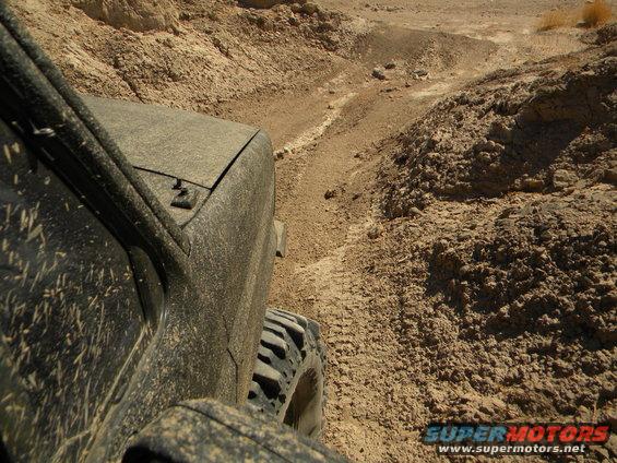 Side view of a dusty off-road vehicle navigating a narrow dirt trail in a desert landscape