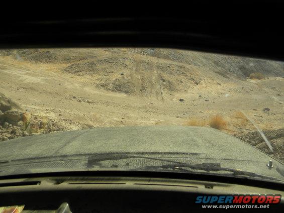 View from inside a dusty vehicle driving on a dirt road in a desert landscape