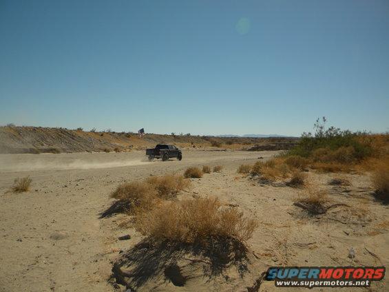 Dark pickup truck driving on a dirt road in a desert landscape, kicking up dust