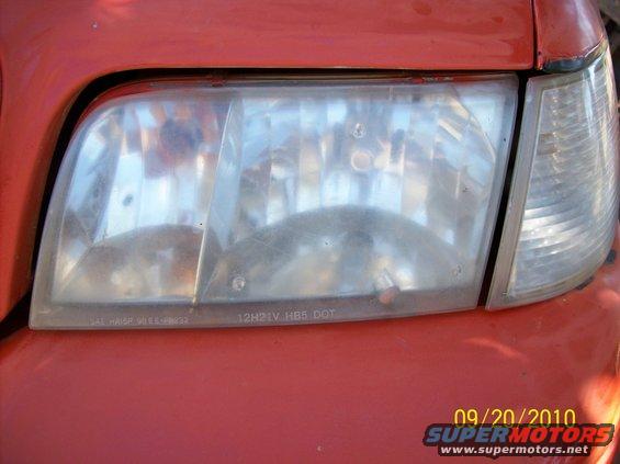 Close-up of a red car's headlight assembly, showing the lens and part of the turn signal