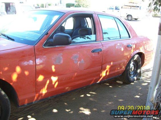 Orange 2002 Ford Crown Victoria sedan, driver's side, showing paint damage and shadows