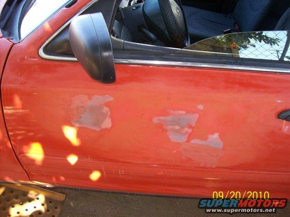 Red car door with peeling paint and black side mirror. 2002 Ford Crown Victoria