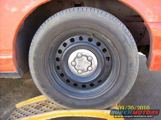 Orange Ford Crown Victoria wheel with a steel rim and a Ford logo on the hubcap, resting on a yellow ramp