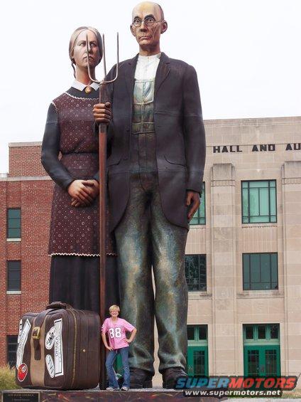 Statue of a farmer and his daughter in front of a building, with a person standing at their feet