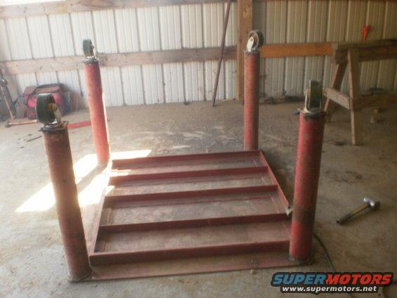 Red metal car lift with four vertical posts and wheels, on a concrete floor