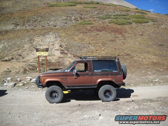 Brown Ford Bronco II with roof rack and spare tire on a dirt road